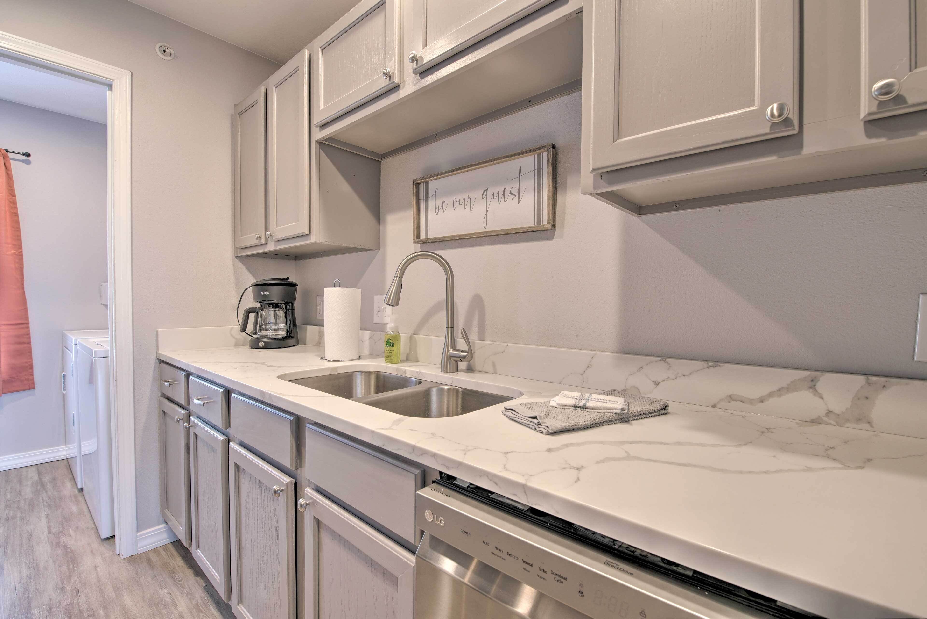A modern kitchen with white cabinetry, a marble countertop, and a built-in dishwasher.