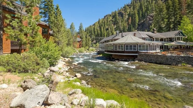 A riverside lodge with a circular building, surrounded by dense forest and rocky terrain. - Updated Condo with River Views! Near Alpine! (Alpine Meadows)