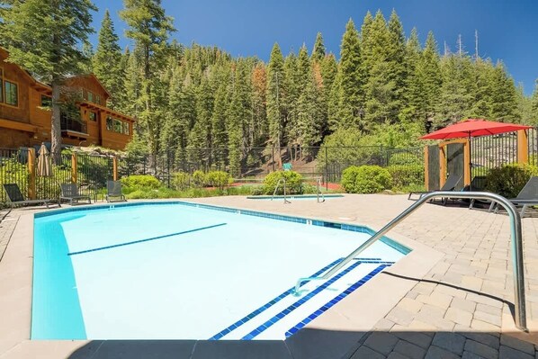 A swimming pool with a blue border, surrounded by a paved deck and a metal fence.