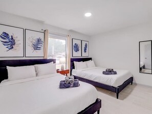 Two single beds with white bedspreads and dark headboards, complemented by framed artworks and a window with a partially drawn curtain.