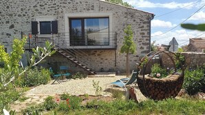 Un bâtiment en pierre doté d’un balcon, d’un espace extérieur aménagé pour s’asseoir et d’un jardin avec des plantes et une structure en bois.
