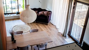 Un salon moderne avec une table à manger en bois, deux chaises, un canapé et un luminaire suspendu.