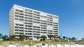 A multi-story hotel with balconies, located near a sandy beach with palm trees. - Extra Large Balcony Overlooking the Beach in Destin w/ Resort Amenities! (Destin)