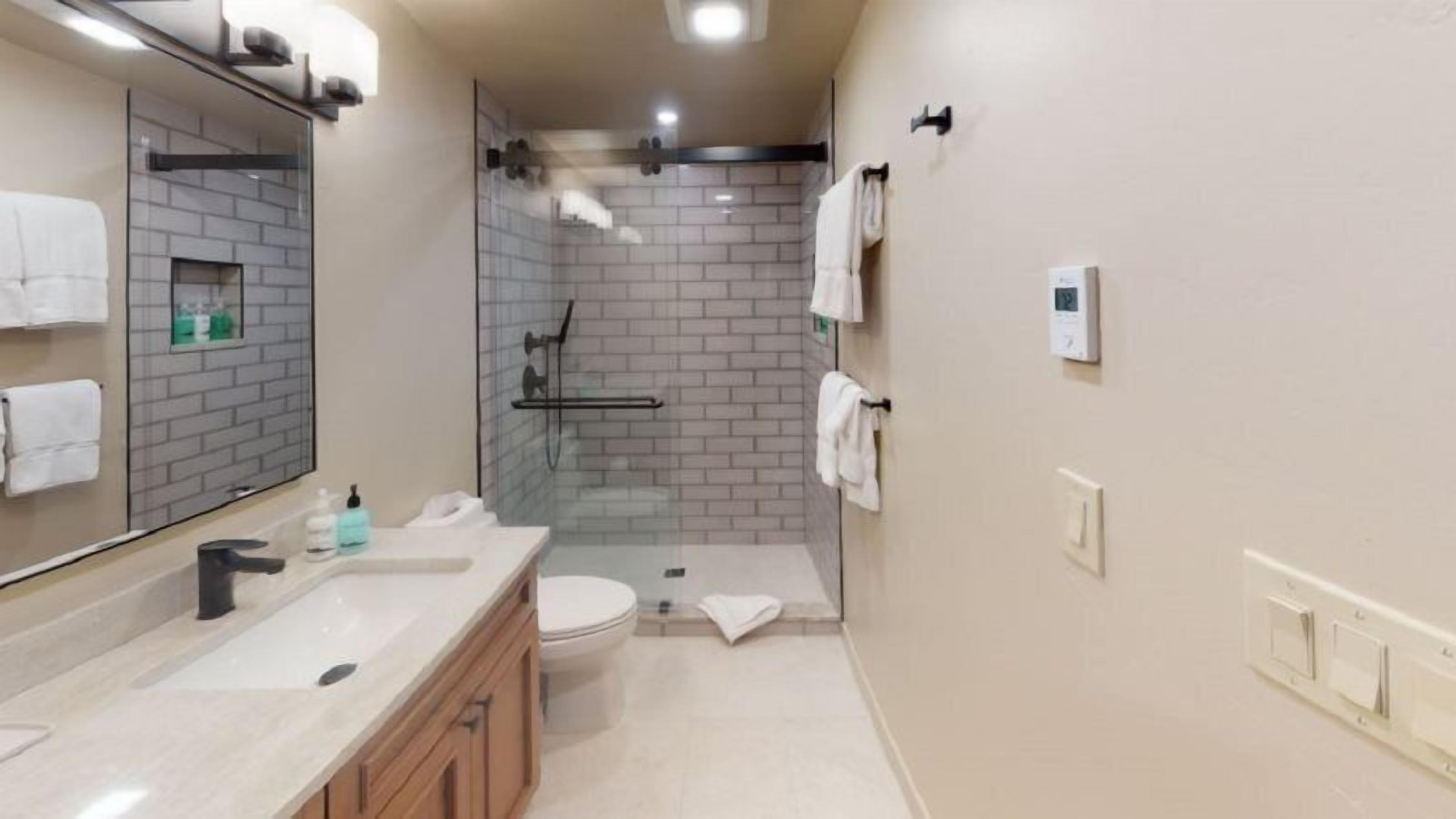 A bathroom with a glass-enclosed shower, a toilet, and a sink with a mirror.