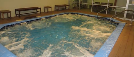 A hot tub with a wooden deck and a glass wall in the background.
