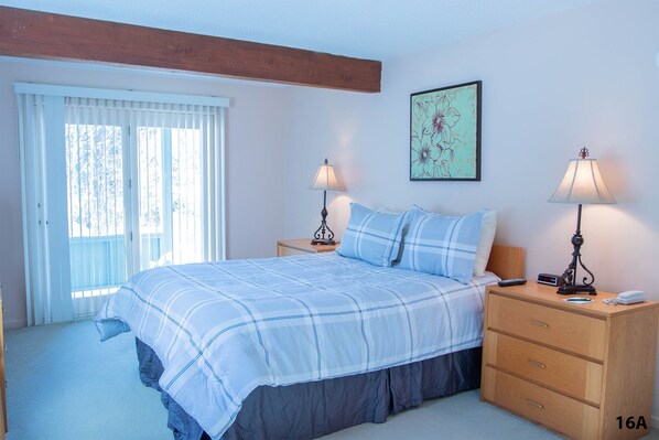 Un dormitorio con una cama, dos mesitas de noche, una lámpara de noche, una ventana con persianas y un cuadro colgado en la pared.