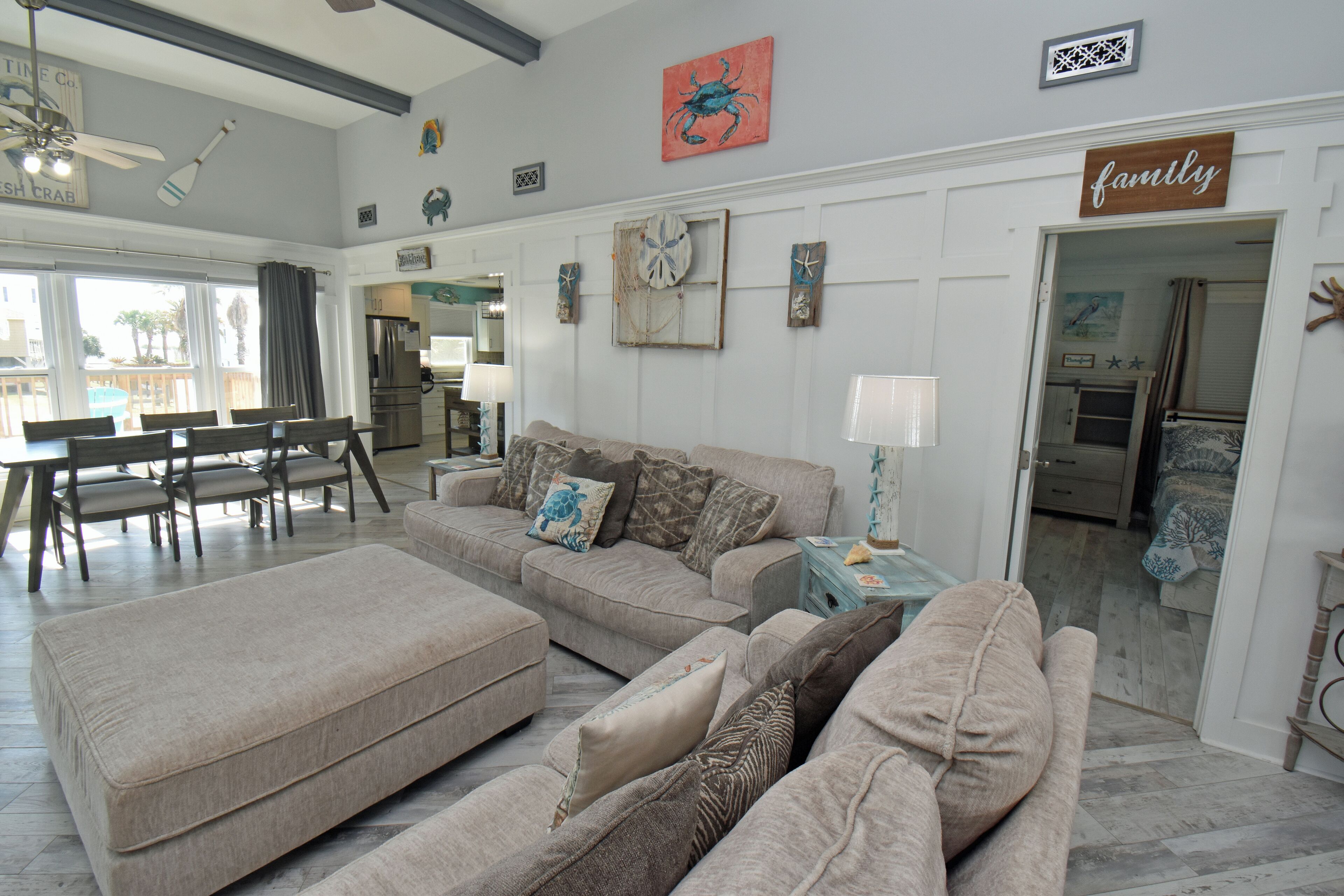 A spacious living room with a beige sectional sofa, a dining area with a wooden table and chairs, and a kitchen visible through an open doorway.
