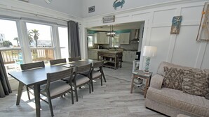 A spacious living area with a dining table, chairs, a sofa, and a kitchen in the background. - Kick's Kids - Channelfront in Garden City Beach! (Garden City Beach)
