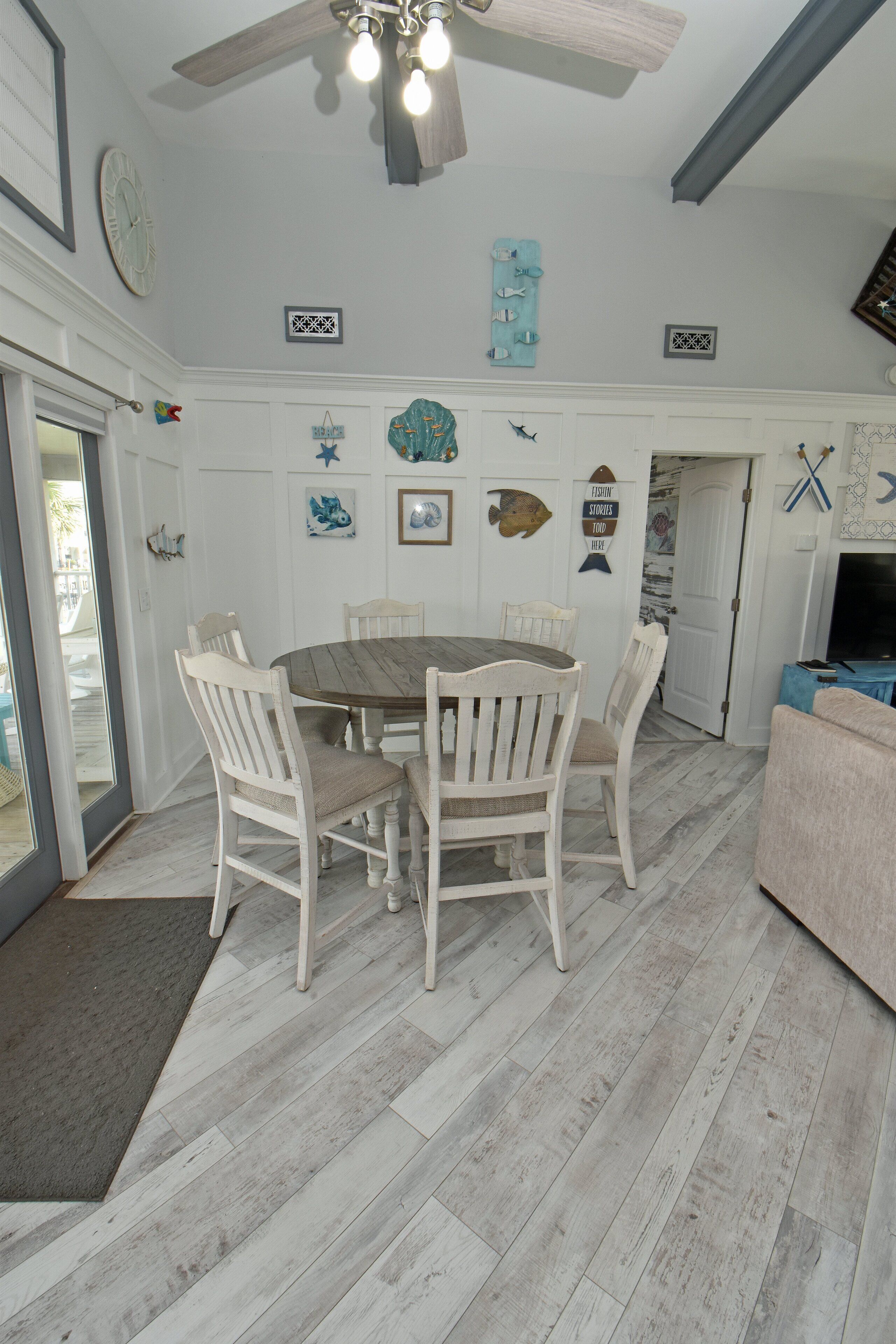 A dining area with a round table and white chairs, a ceiling fan, and wall decorations including fish and a star.