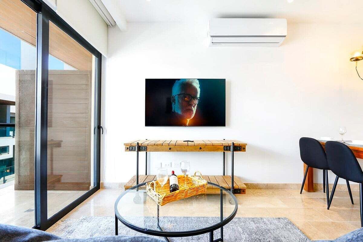 Een moderne woonkamer met een glazen tafel, een houten bank en een tv aan de muur.