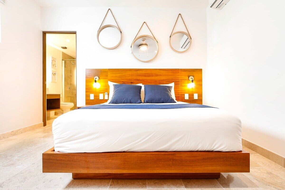 Una habitación de hotel moderna con estructura de cama de madera, ropa de cama blanca y tres espejos colgados en la pared.