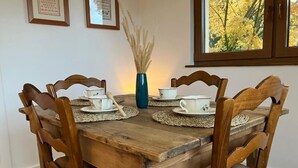 Une table à manger en bois, accompagnée de quatre chaises, un vase contenant des plantes séchées et des tableaux encadrés accrochés au mur.