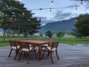 Um deck de madeira com mesa e cadeiras, rodeado por árvores e uma paisagem montanhosa.