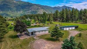 A rural property with a large house, a fenced-in area, and a mountain backdrop. - 3/2 home 20 minutes from Glacier National Park, Sleeps 8! (Columbia Falls)
