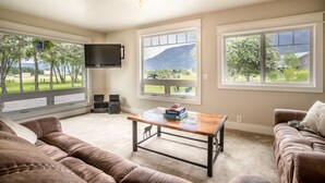 A living room with a large window, a flat-screen TV, a wooden coffee table, and a brown leather couch. - 3/2 home 20 minutes from Glacier National Park, Sleeps 8! (Columbia Falls)
