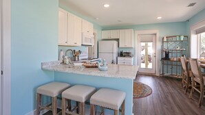 A kitchen with a central island, white cabinets, and a dining area with chairs and a table. - 175 Steps from the Beach, Sweeping Views, Ground Floor (Mexico Beach)