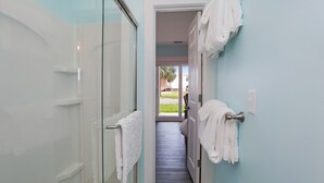 A bathroom with a glass shower enclosure, a towel rack, and a view of a backyard through an open door. - 175 Steps from the Beach, Sweeping Views, Ground Floor (Mexico Beach)