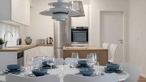 Una cocina moderna con horno empotrado y comedor con mesa blanca para cuatro.