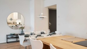 Un comedor moderno con un espejo redondo, sillas blancas, una mesa de madera y una lámpara colgante.