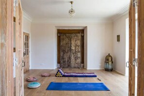 A room with wooden flooring, a blue yoga mat, and a patterned cushion.