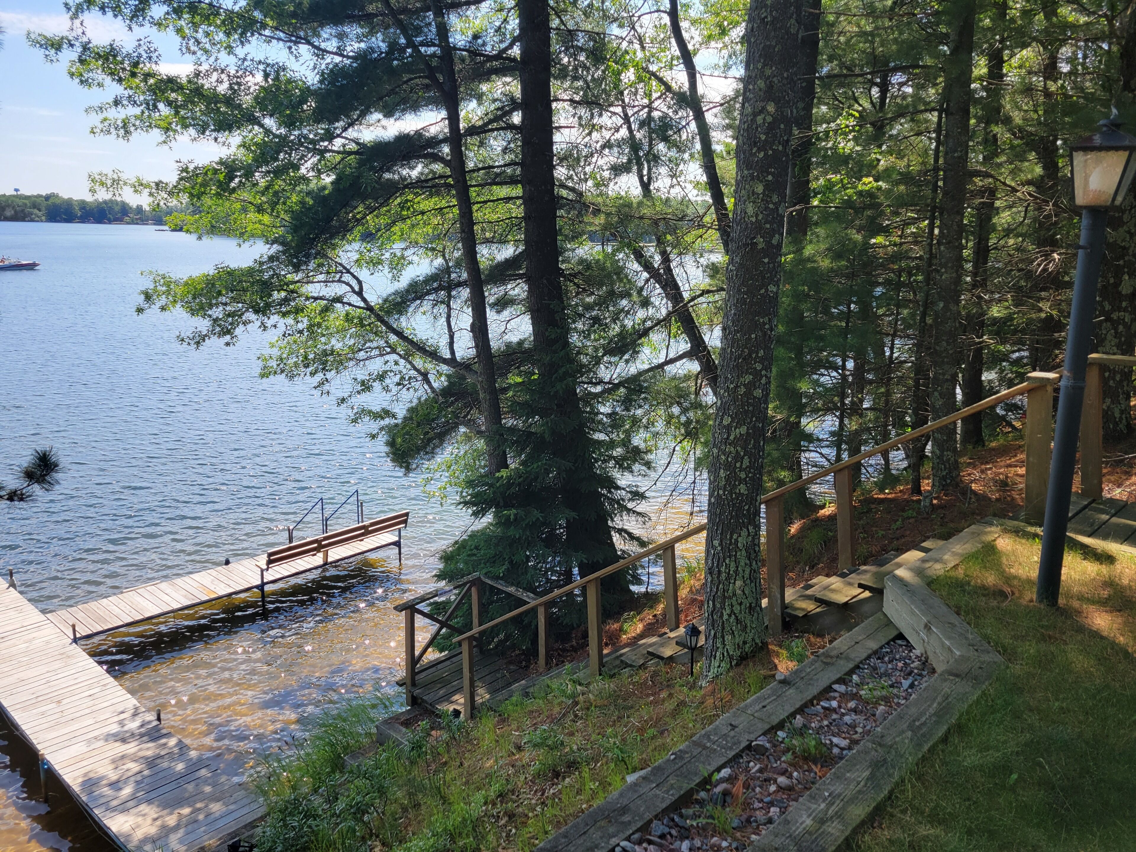 A wooden dock extending into a calm lake, surrounded by dense trees and a wooden staircase leading down to the water.