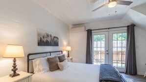 A bedroom with a bed, two bedside lamps, a ceiling fan, a painting, and a view through a glass door.
