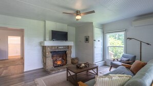 A cozy living room with a stone fireplace, wooden furniture, and a ceiling fan.