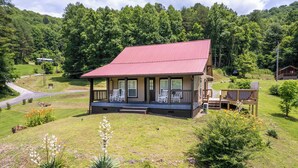A lodge with a red roof, a porch with chairs, and a view of a forested area.