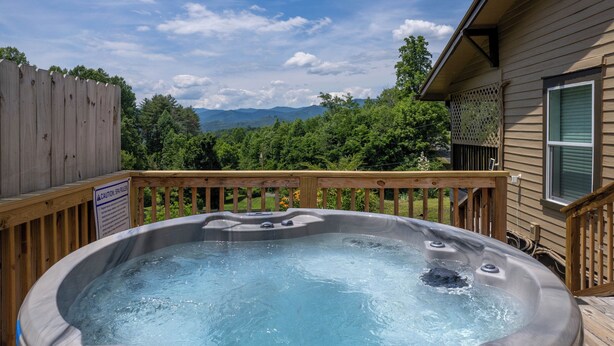 A hot tub on a wooden deck with a view of mountains and trees.