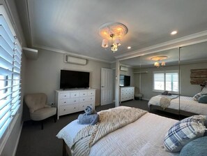 Un dormitorio con cama, una silla, cómoda, televisor y espejo.