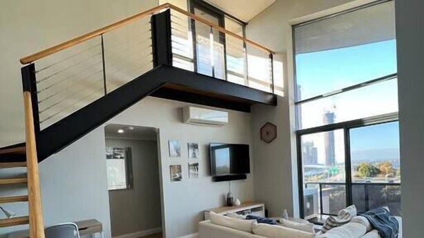 Een moderne woonkamer met een trap, een witte bank, een televisie en uitzicht op de stad.