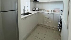 Een kleine keuken met witte kasten, een roestvrijstalen koelkast, een magnetron en een waterkoker.