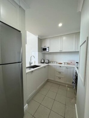 A compact kitchen with white cabinets, a stainless steel refrigerator, a microwave, and a kettle.