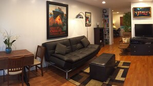 A compact living space with a sofa, a dining table, a TV, and a kitchenette.