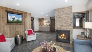 A modern living room with a fireplace, stone wall, and a television mounted on a wooden panel. - Lockoff room in heart of Lionshead Village W208B (Vail)