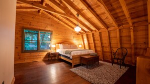 Une chambre à coucher dans une cabane en bois, avec un lit, des tables de chevet, une chaise et une fenêtre donnant sur la forêt.