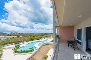 Un balcon avec vue sur la piscine, un coin repas et une vue sur la plage et les montagnes.