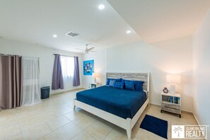 Une chambre à coucher avec un lit, des rideaux, un ventilateur de plafond, une table de chevet et une œuvre d’art murale.