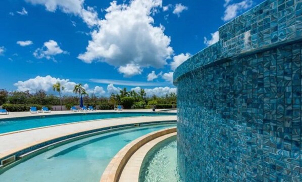 A pool area with clear blue water, a tiled wall, and lounge chairs.