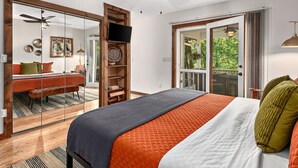 Ein Schlafzimmer mit Bett, Deckenventilator, Fernseher und einer Schiebetür zum Balkon.