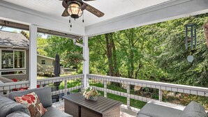 Ein überdachter Außenbereich mit Deckenventilator, einem Tisch mit einer Vase und Blick auf einen Garten.