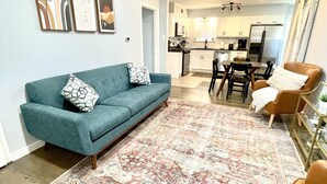 A modern living room with a teal sofa, a patterned rug, and a brown leather chair.