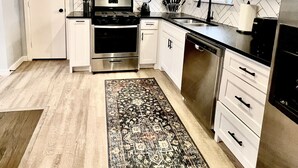 A modern kitchen with white cabinets, stainless steel appliances, and a patterned rug.