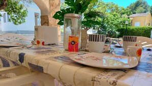 A table set with plates, cups, and a candle holder, surrounded by chairs and a potted plant. - Spacious villa close to the beach and the forest (L'Escala)