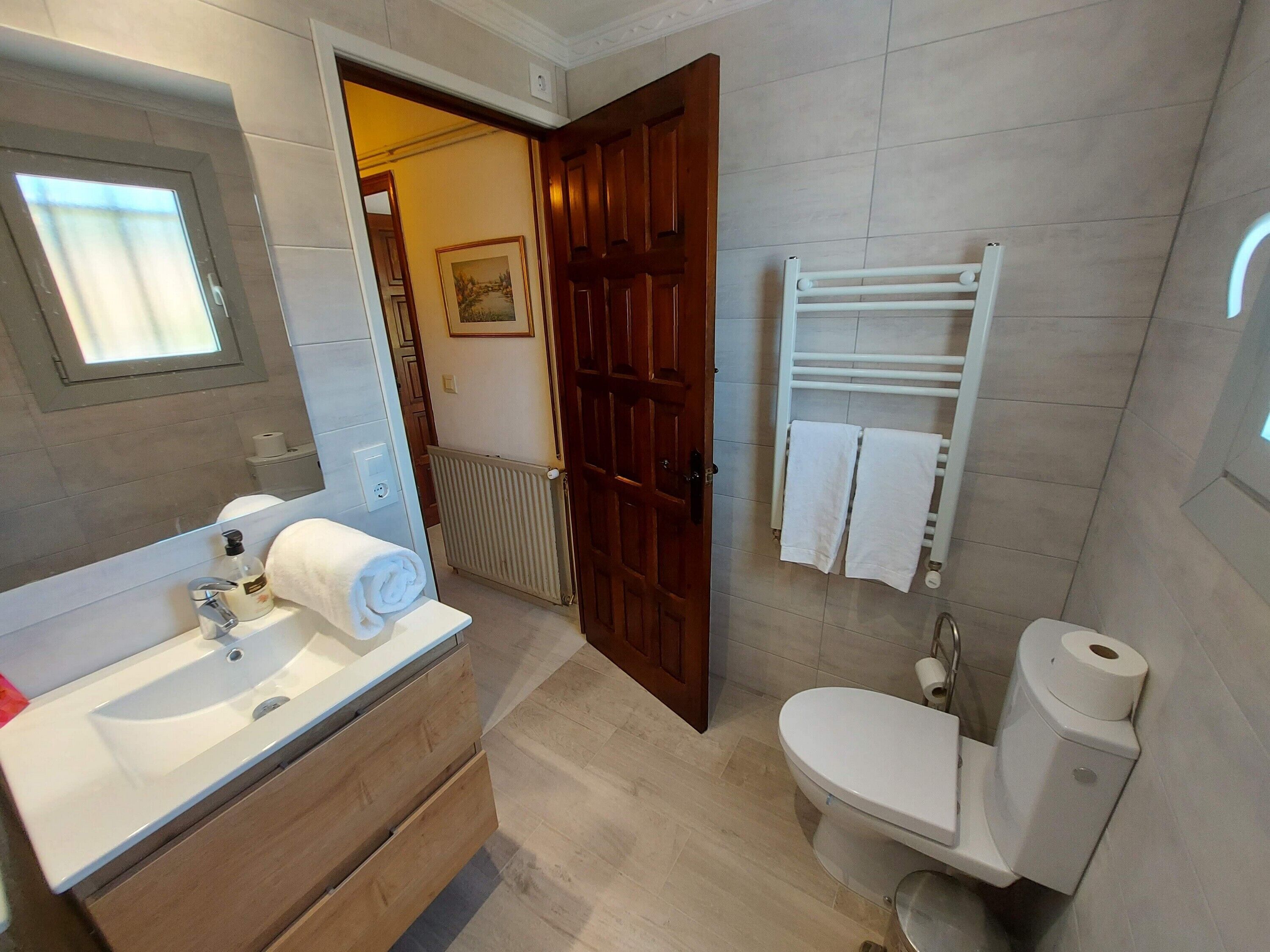 Une salle de bain avec un meuble-lavabo en bois, un lavabo blanc, un miroir, des toilettes et un porte-serviettes.