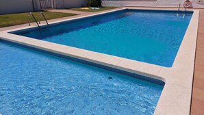 A rectangular swimming pool with clear blue water, surrounded by a tiled deck and a white wall. - Spacious villa close to the beach and the forest (L'Escala)