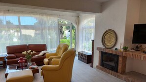 A living room with a brown leather sofa, two yellow armchairs, a small ottoman, a glass coffee table, and a fireplace. - Spacious villa close to the beach and the forest (L'Escala)