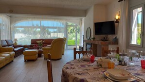 A spacious living room with a large sofa, a coffee table, and a dining area with a table set for two. - Spacious villa close to the beach and the forest (L'Escala)