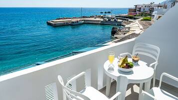 A balcony with white chairs and a table set with fruit and drinks, overlooking a marina and the sea.