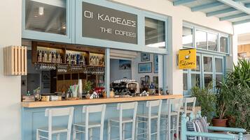 A café with a bar area, white bar stools, and a sign reading "OI KAFEAS THE COFES".